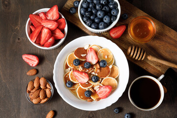 Fototapeta na wymiar Mini pancakes cereal bowl with berries on wooden background