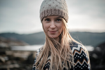 Nice close portrait of a young blodne woman smiling to a camera wearing a handmade knitted hat on a nice sunny spring evening
