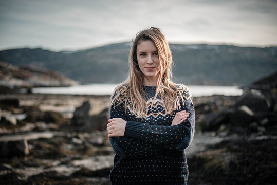 Beautiful young woman is smiling to camera with her hands crossed. Wearing norwegian style sweater on a nice spring day