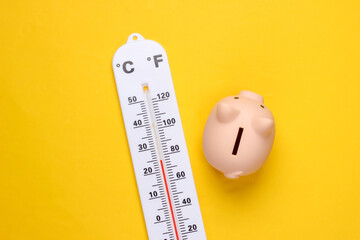 Piggy bank and weather thermometer on yellow background. Minimalistic studio shot. Overhead view. Flat lay. - obrazy, fototapety, plakaty