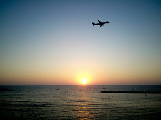 Silhouette of plane flying over Tel Aviv beach at sunset. Golden sky and sea