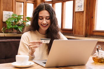 Image of woman using laptop and holding credit card while drinking tea