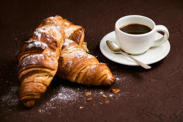 Still life with cup of fresh coffee and delicious butter croissants on dark brown board