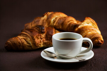 Still life with cup of fresh coffee and delicious butter croissants on dark brown board