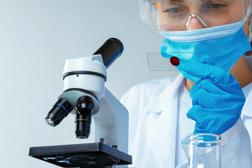 Woman scientist looking at slide with blood sample near microscope in laboratory