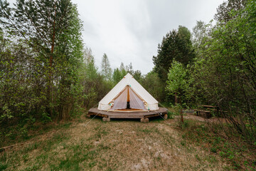 Rest place in forest: lonely glamping tent on a wooden floor among green trees in Pleshcheyevo Ozero National Park