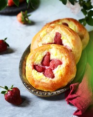 Homemade buns with cottage cheese and strawberries (cheesecakes) in a dish on a gray background, Russian cuisine