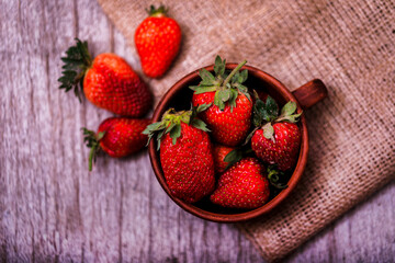 Small bowl filled with succulent juicy fresh ripe red strawberries on an old wooden textured table top. Fresh juicy organic strawberries in an old clay bowl.