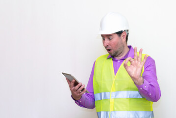 Construction builder wearing helmet yellow protective vest using wireless tablet and showing like or thumbs-up shocked poke up shows to you and victory  gesture isolated on white background.