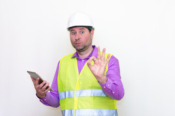 Construction builder wearing helmet yellow protective vest using wireless tablet and showing like or thumbs-up shocked poke up shows to you and victory  gesture isolated on white background.