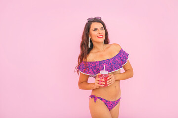 Fototapeta na wymiar Portrait of happy young woman in swimsuit with cocktail on pink background