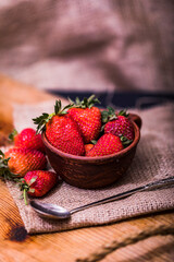 Fresh strawberries in a bowl on wooden table with low key scene.