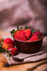 Fresh strawberries in a bowl on wooden table with low key scene.