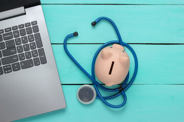 Laptop with piggy bank, stethoscope on a blue background. Online doctor. Top view. Flat lay
