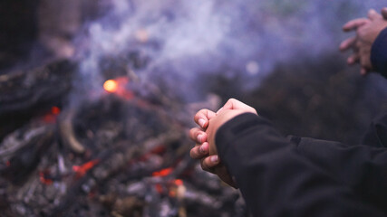 Naklejka premium Hands of the tourists and trekkers near the bonfire, camping fire in the forest after long trekking, dinner time on the trek, warmth in the evening in the forest and mountains