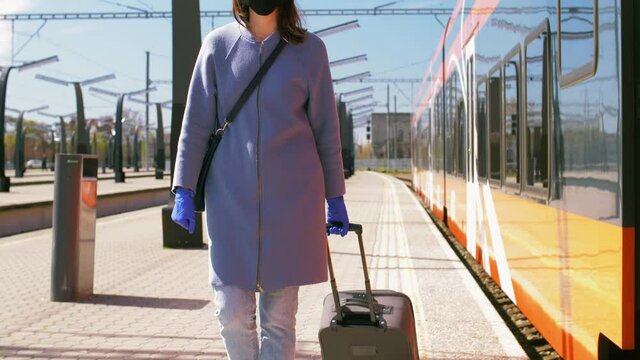health, safety and pandemic concept - young woman in protective black face mask with travel bag walking along empty railway station