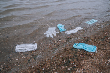 garbage from used medical masks and gloves on the beach and in the water - Powered by Adobe