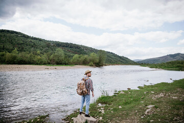 Man tourist with a backpack travels along the mountain river. Copy spase