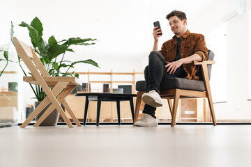 Image of joyful young man smiling and using cellphone while working