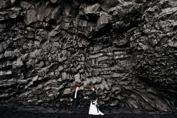 Destination Iceland wedding. Wedding couple under a rock of basalt stones. Bride and groom on the...