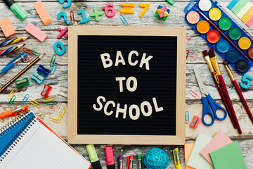 The words Back to School written in chalk on school desk with school supplies close-up.