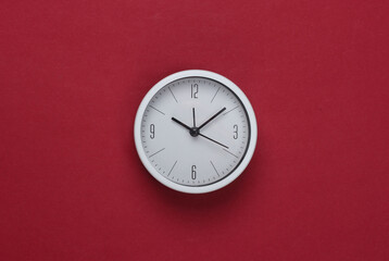 White clock on red background. Minimalistic studio shot. Top view
