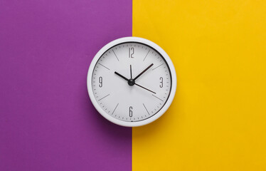 White clock on purple yellow background. Minimalistic studio shot. Top view