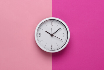 White clock on pink pastel background. Minimalistic studio shot. Top view