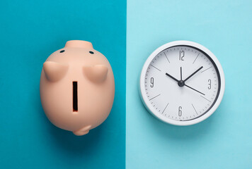 Time to invest. White clock and piggy bank on blue background. Minimalistic studio shot. Top view