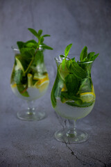 Summer mint lime refreshing cocktail mojito with rum and ice in glass on gray background. Mojito cocktail on stone table. Glassy high glass for drinks. Lemonade at the bar.