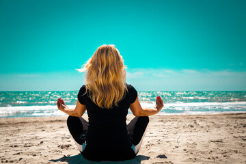 Beautiful young woman is sitting on a sandy beach in meditation pose doing yoga