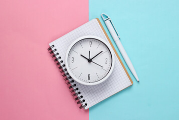 White clock and notebook on pink blue pastel background. Minimalistic studio shot. Top view