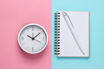 Fototapeta na wymiar White clock and notebook on pink blue pastel background. Minimalistic studio shot. Top view
