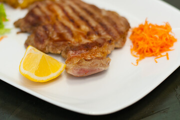 Juicy and delicious grilled meat steak with lemon, carrots, lettuce and potatoes.
