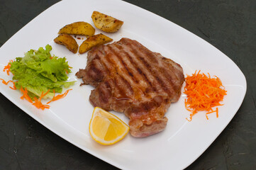 Grilled meat steak with lemon, carrots, lettuce and potatoes. Juicy and very tasty dish of Italian cuisine