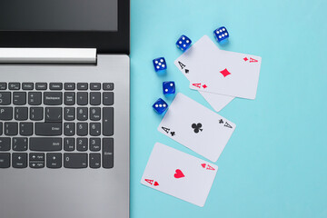 Four aces, dice and laptop keyboard on a blue background. Online poker casino. Game addiction