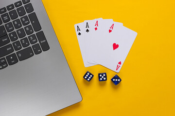 Four aces, dice and laptop keyboard on yellow background. Online poker casino. Game addiction. Top view