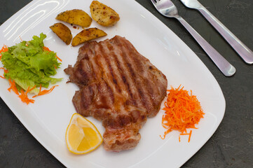 Grilled beef or veal meat steak with lemon, carrots, lettuce and potatoes. Juicy and very tasty dish of Italian cuisine