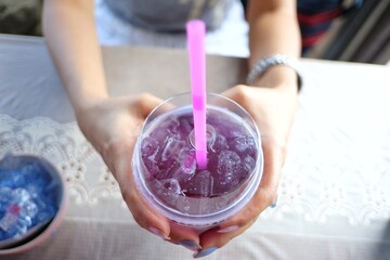 Close up  a woman hands holding a glass of butterfly-pea juice on ice with  dining table background 