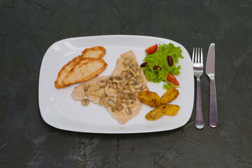 Stewed mushrooms with fish fillet, salad, fried potatoes and croutons, on a warm gray background. Tasty traditional italian food