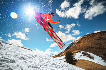 A young stylish man in sunglasses and a cap performs a trick in jumping with a kicker of snow...