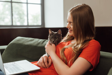 happy freelancer using laptop and touching cute cat in living room