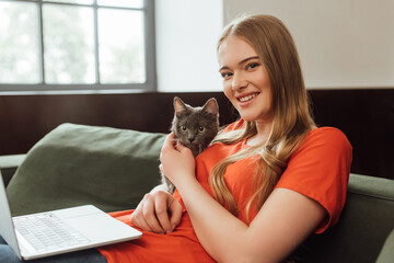 Obraz premium happy freelancer touching cute cat near laptop in living room