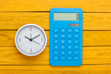 White clock and calculator on yellow wooden background. Minimalistic studio shot. Top view