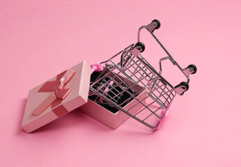 Supermarket trolley in a gift box on a pink background.