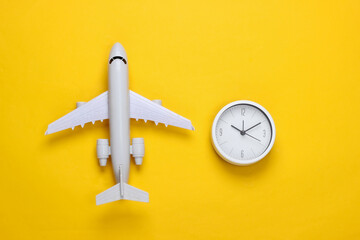 Time to travel. Plane figurine and clock on a yellow background. Top view