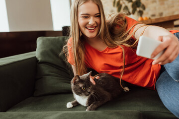 selective focus of smiling young woman taking selfie with cat