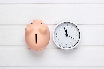 Time to invest. White clock and piggy bank on white wooden background. Top view