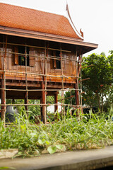 Wooden brown house with a red tile roof on stilts on a river bank in Asia