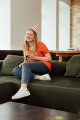 Obraz premium selective focus of happy woman in party cap sitting on sofa and holding glass of red wine